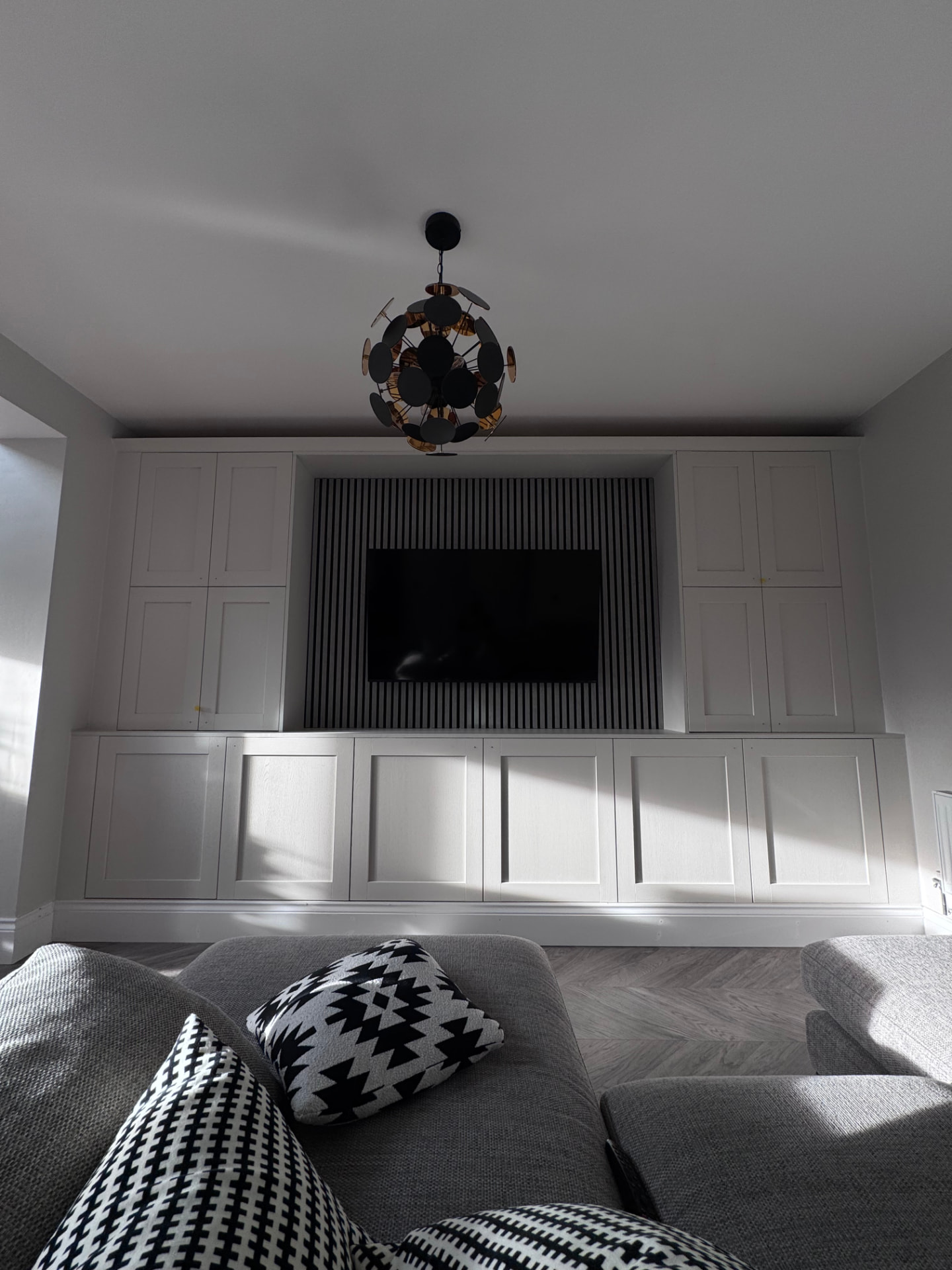 Fitted media wall with white shaker cabinetry and black slatted TV panel