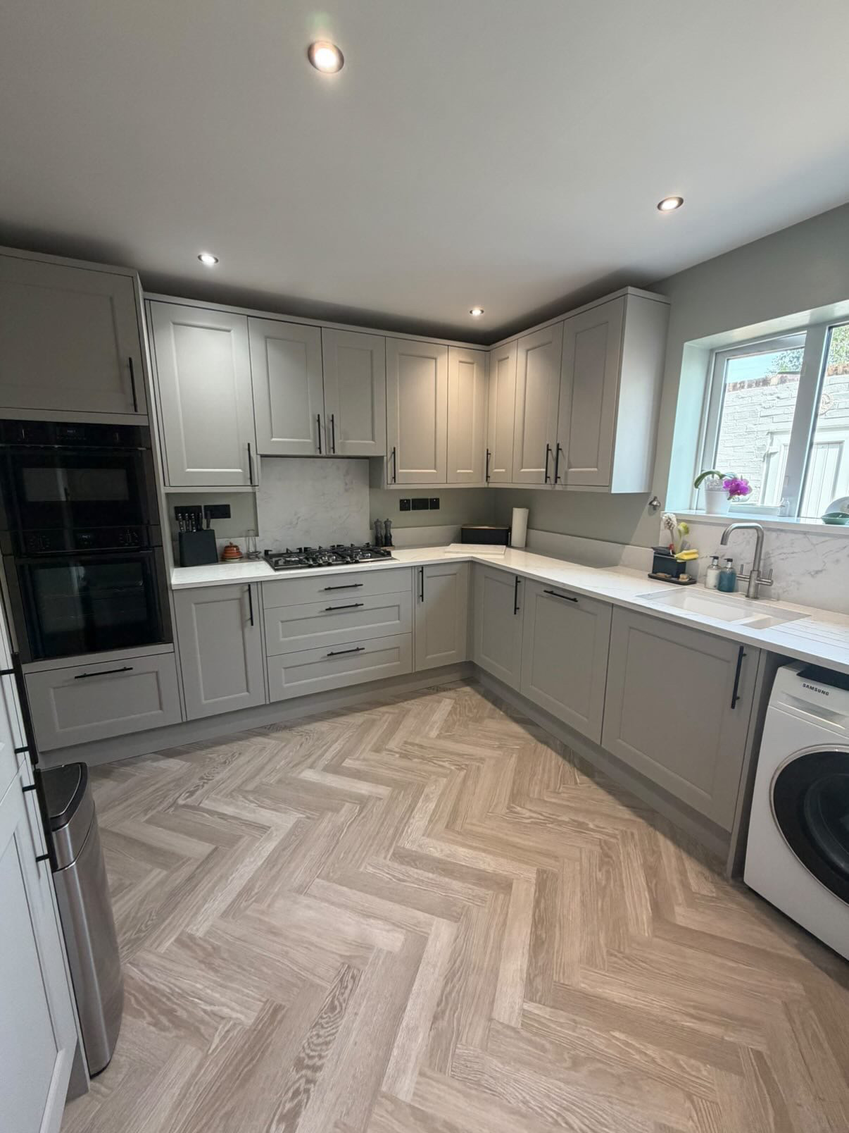 Light grey shaker kitchen with white quartz worktops and herringbone flooring