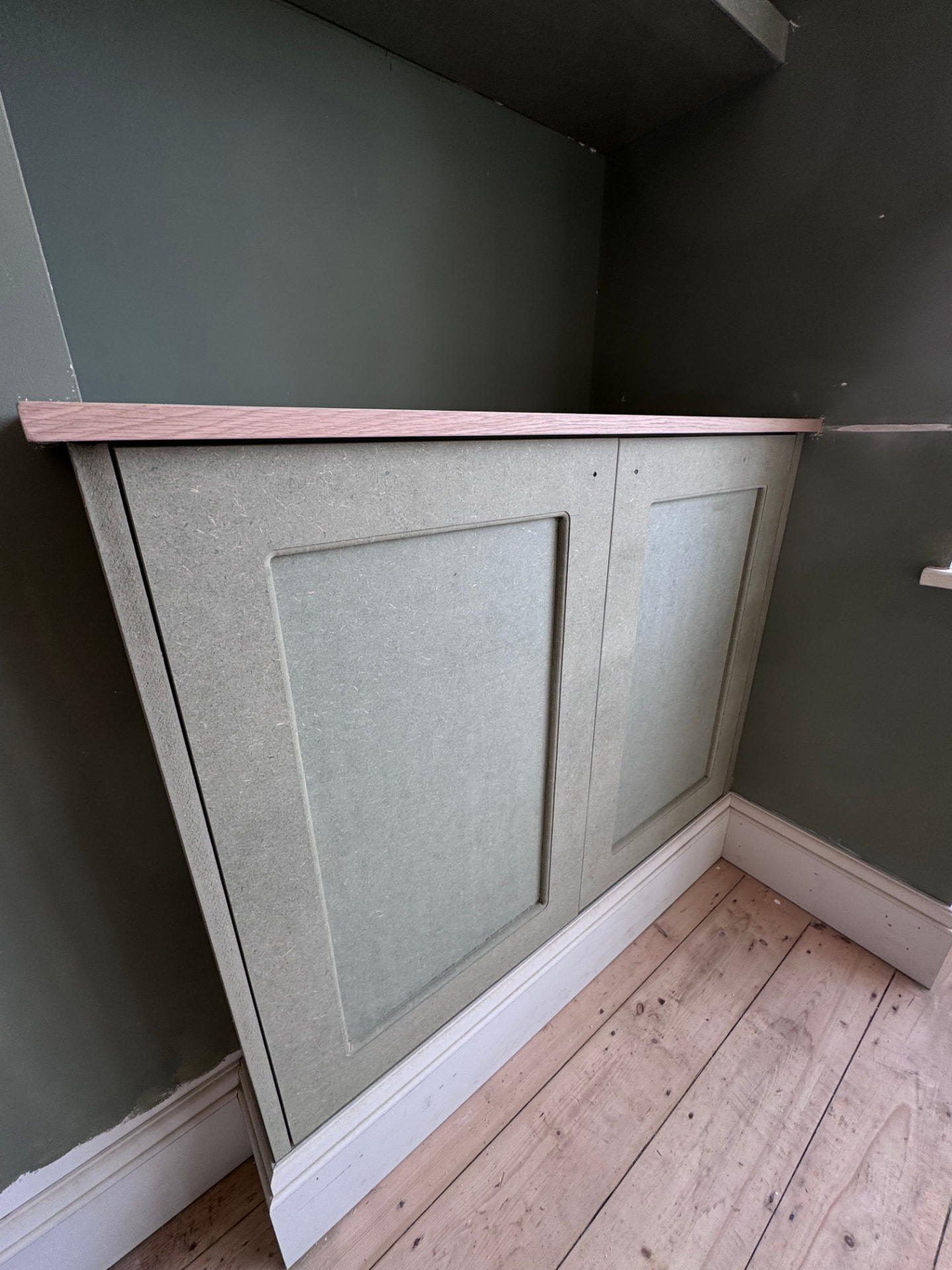 Bespoke sage green fitted wardrobe with panelled doors under a sloped ceiling