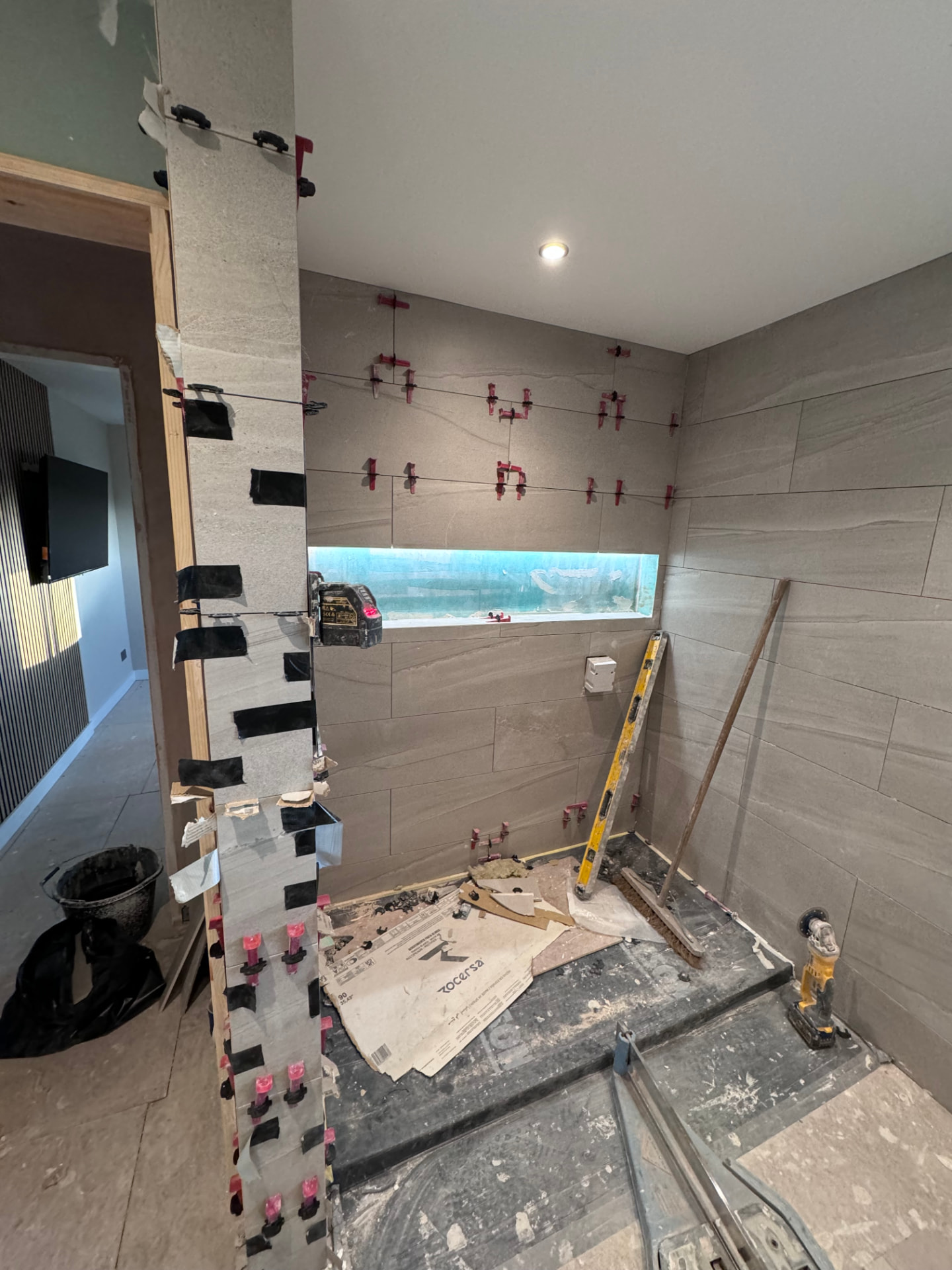 Family bathroom being tiled with a lit shower niche and laser level set up