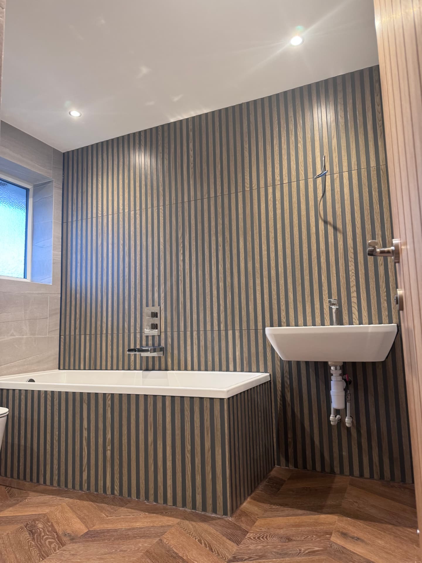Finished family bathroom with slatted panelling, bath and wall-hung basin