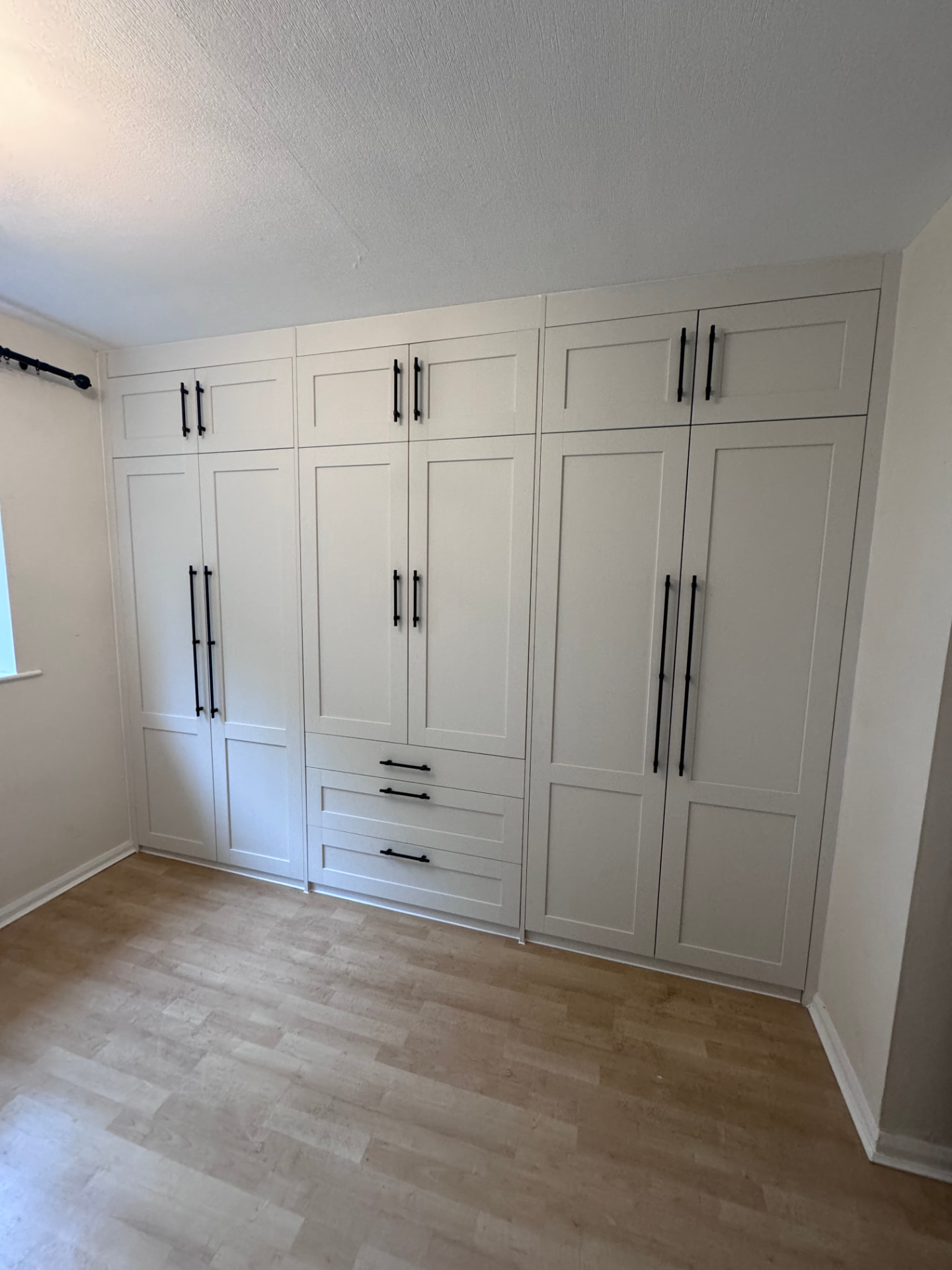 Full wall of white shaker fitted wardrobes with black bar handles